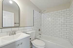 Full bathroom featuring decorative backsplash, vanity, tiled shower / bath combo, tile walls, and toilet