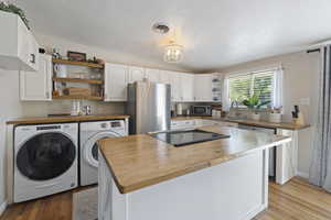 Kitchen with stainless steel appliances, sink, washing machine and clothes dryer, light hardwood / wood-style floors, and white cabinetry