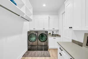 Laundry room featuring washing machine and dryer, sink, cabinets, and light wood-type flooring