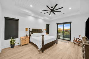 Bedroom with access to exterior, light wood-type flooring, a tray ceiling, and ceiling fan