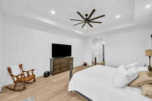 Bedroom with light hardwood / wood-style flooring, a raised ceiling, ceiling fan, and wood ceiling