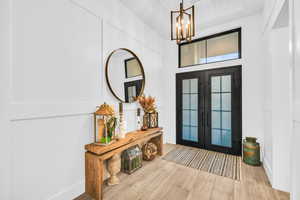 Foyer entrance with french doors, a high ceiling, a notable chandelier, and light wood-type flooring