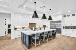 Kitchen featuring a kitchen island with sink, hanging light fixtures, light wood-type flooring, a tray ceiling, and stainless steel appliances