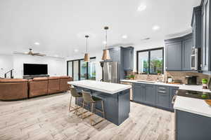 Kitchen featuring light wood-type flooring, backsplash, stainless steel appliances, a center island, and hanging light fixtures