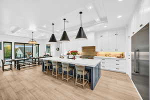 Kitchen with appliances with stainless steel finishes, a raised ceiling, a large island with sink, pendant lighting, and white cabinets