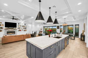 Kitchen with light stone countertops, a wealth of natural light, sink, decorative light fixtures, and an island with sink