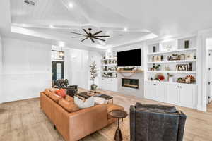 Living room featuring beam ceiling, built in shelves, ceiling fan, and light wood-type flooring