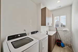 Clothes washing area with washer and dryer, cabinets, and light hardwood / wood-style flooring