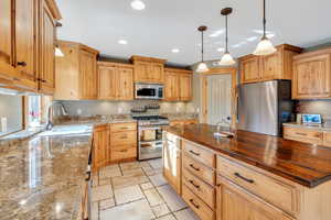 Kitchen featuring a center island, hanging light fixtures, sink, appliances with stainless steel finishes, and butcher block countertops