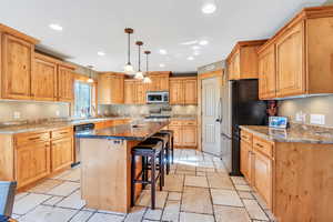 Kitchen with a center island, light stone countertops, appliances with stainless steel finishes, decorative light fixtures, and a breakfast bar area