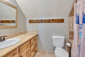 Bathroom with tile patterned floors, lofted ceiling, a textured ceiling, toilet, and vanity