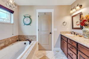 Bathroom with tile patterned floors, tiled bath, vanity, and an inviting chandelier