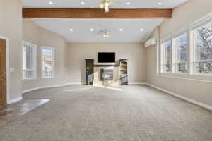 Unfurnished living room featuring a wall mounted air conditioner, ceiling fan, lofted ceiling with beams, and a wealth of natural light