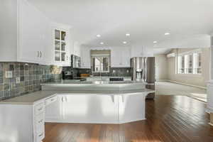 Kitchen featuring kitchen peninsula, black appliances, wood-type flooring, white cabinetry, and plenty of natural light