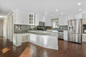 Kitchen with kitchen peninsula, dark hardwood / wood-style flooring, stainless steel appliances, crown molding, and white cabinetry