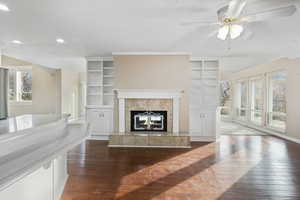 Living room with a fireplace, built in features, ceiling fan, and dark wood-type flooring