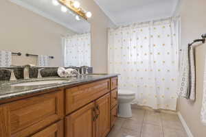 Bathroom featuring tile patterned floors, a shower with curtain, vanity, crown molding, and toilet