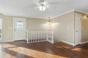 Entrance foyer featuring ceiling fan with notable chandelier, wood-type flooring, and ornamental molding