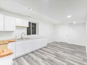 Kitchen featuring butcher block countertops, white cabinets, light wood-type flooring, and sink