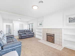 Living room featuring built in shelves, light colored carpet, and a tile fireplace