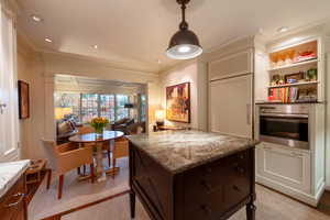 Kitchen with light stone countertops, dark brown cabinets, oven, and ornamental molding