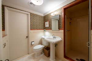 Bathroom with toilet, a tile shower, and crown molding