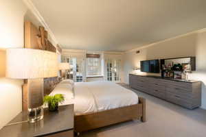 Carpeted bedroom with ornamental molding and french doors