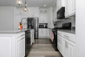 Kitchen with light wood-type flooring, sink, black appliances, decorative light fixtures, and white cabinetry