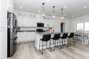 Kitchen featuring appliances with stainless steel finishes, sink, white cabinets, hanging light fixtures, and an island with sink