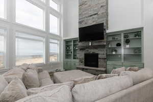 Living room with a stone fireplace, a towering ceiling, a healthy amount of sunlight, and wood-type flooring