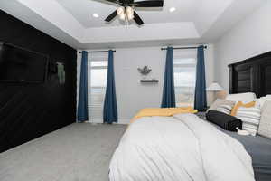 Carpeted bedroom with ceiling fan and a tray ceiling