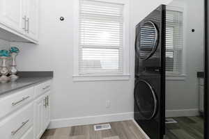 Washroom with stacked washer / dryer, cabinets, and light wood-type flooring