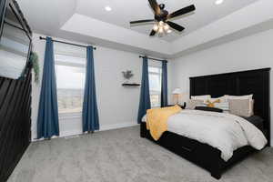 Bedroom featuring a tray ceiling, ceiling fan, and light carpet