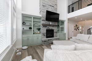 Living room featuring a towering ceiling, hardwood / wood-style flooring, a stone fireplace, and a wealth of natural light