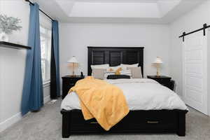 Bedroom featuring carpet, a barn door, and a raised ceiling