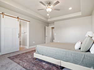 Carpeted bedroom with a barn door, a raised ceiling, and ceiling fan