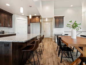 Kitchen featuring light stone countertops, hanging light fixtures, dark brown cabinets, a kitchen island, and light wood-type flooring