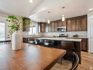 Kitchen featuring pendant lighting, light stone countertops, appliances with stainless steel finishes, and vaulted ceiling