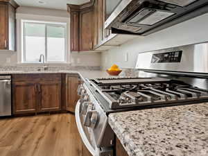 Kitchen featuring light stone countertops, light wood-type flooring, dark brown cabinetry, stainless steel appliances, and sink