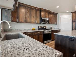 Kitchen featuring sink, light stone countertops, stainless steel appliances, and light wood-type flooring