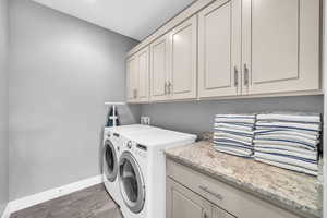 Clothes washing area featuring cabinets, wood-type flooring, and washing machine and clothes dryer