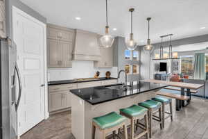 Kitchen with a kitchen breakfast bar, premium range hood, stainless steel appliances, sink, and wood-type flooring