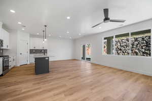 Kitchen featuring hanging light fixtures, appliances with stainless steel finishes, a center island with sink, white cabinets, and light wood-type flooring