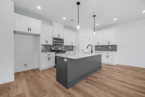 Kitchen featuring pendant lighting, a kitchen island with sink, white cabinets, light wood-type flooring, and appliances with stainless steel finishes