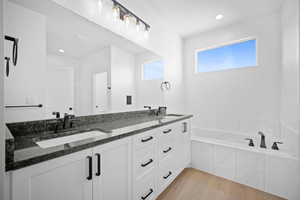 Bathroom with tiled tub, vanity, and hardwood / wood-style flooring