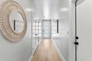Hallway featuring light wood-type flooring, baseboards, recessed lighting, and a textured ceiling