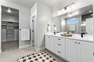 Full bath with double vanity, tile patterned flooring, a walk in closet, baseboards, and a shower