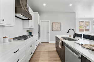Kitchen with premium range hood, appliances with stainless steel finishes, a sink, decorative backsplash, and white cabinets