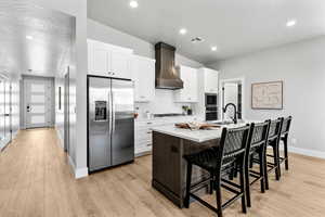 Kitchen featuring stainless steel appliances, custom exhaust hood, a center island with sink, white cabinets, and a breakfast bar area