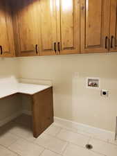 Washroom with hookup for an electric dryer, cabinets, light tile patterned floors, and hookup for a washing machine